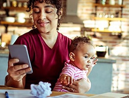 Smiling mom looking at her mobile while holding her 2 month old