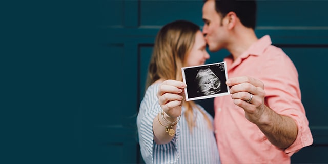 Pregnant mom and dad holding a ultrasound photo of their baby